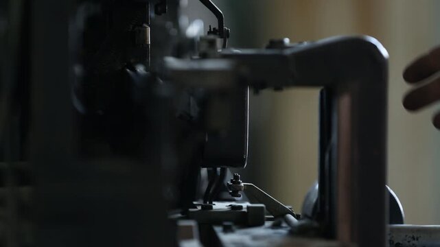Skilled worker adjusts and maintains complex vintage printing press or typesetting machine. Detailed close-up of hands on intricate industrial components and levers.