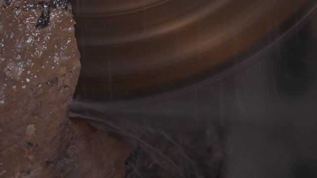 Close-up of a large diamond saw cutting a natural stone block in a factory. Water cools the blade and suppresses dust during the industrial marble or granite processing.

