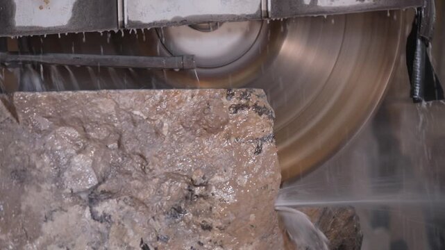 Close-up of a large diamond saw cutting a natural stone block in a factory. Water cools the blade and suppresses dust during the industrial marble or granite processing.

