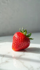 Single red strawberry rests on a white marble surface. Sunlight creates shadows and highlights on the fruit and table. Fresh berry shows its texture and vibrant color.