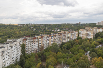 Fototapeta premium Panoramic city view showing residential apartment buildings and green forest hills under cloudy autumn sky in Chisinau,