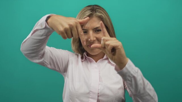 Woman confidently framing view with her precise focused hands in a teal studio setting; creativity perspective.