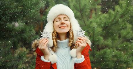 Winter day, happy smiling young woman enjoys snow, warm weather against Christmas tree background