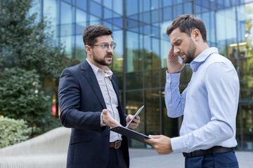 Two businessmen having an intense argument and conflict outdoors, one appearing stressed and...