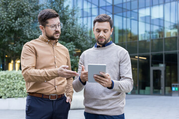 Two professional businessmen discussing a new marketing strategy and analyzing data on a digital...