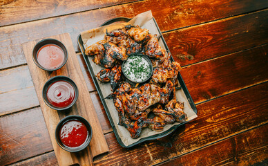 A tray of chicken wings is served on a wooden table with three condiment cups