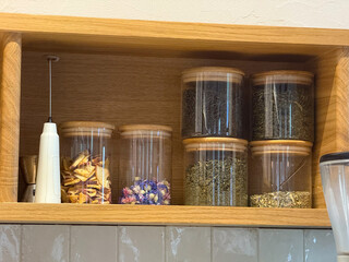 Glass jars with dried herbs and fruits on wooden shelf. Natural ingredients, tea blends and cozy cafe interior atmosphere.