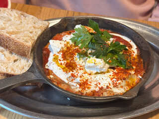 Shakshuka with bread served in iron skillet. Mediterranean flavor, freshness, and homemade comfort in cafe breakfast dish.