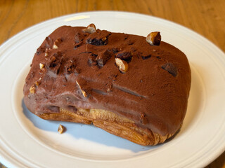 Chocolate-covered pastry with nuts on white plate. Sweetness, texture, and indulgence in artisanal dessert presentation.