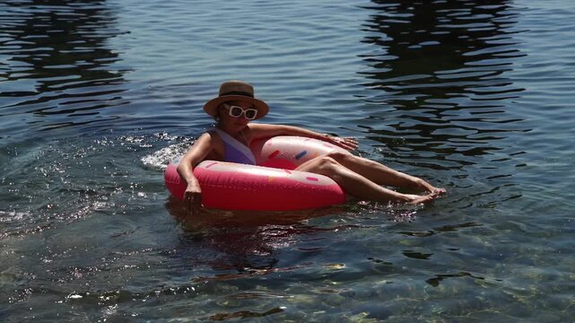 Woman Float Water: Woman relaxing on pink donut float in clear water under bright summer sun.