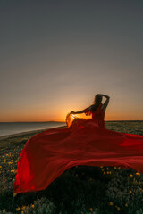 Dress Woman Sunset: Woman in red dress poses at sunset on flowery beach for artistic photography.