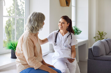 Obraz premium Senior woman patient in medical clinic talking with female young friendly doctor wearing stethoscope sitting on couch in office during examination. Doctor support and health care concept.