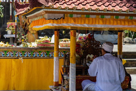 Balinese man praying at a vibrant temple shrine with offerings, promoting peace and cultural beauty for travel brochures and spiritual growth content