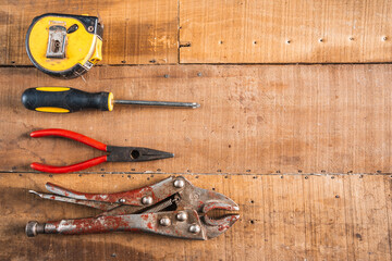 Antique construction tools, such as an old wooden level, a wooden plane, pliers, and a plumb line, are isolated and display an antique charm on a brown wooden wall.