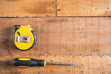 Antique construction tools, such as an old wooden level, a wooden plane, pliers, and a plumb line, are isolated and display an antique charm on a brown wooden wall.