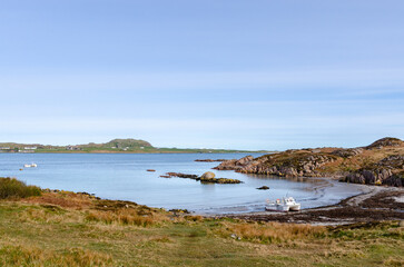 Peaceful coastal bay with clear blue water, gentle waves, and rocky shoreline surrounded by grassy hills on the Isle of Mull, Scotland.