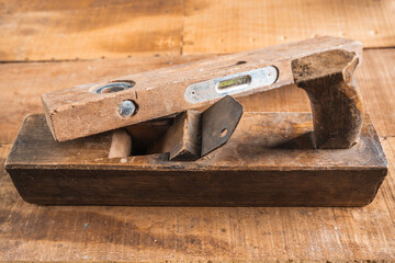 Antique construction tools, such as an old wooden level, a wooden plane, pliers, and a plumb line, are isolated and display an antique charm on a brown wooden wall.