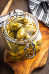 Pickled capers berries in jar on wooden cutting board.