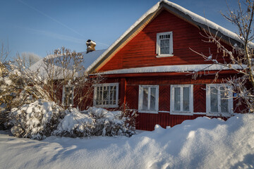 Charming red wooden house blanketed in snow under a crisp blue sky &mdash; cozy, picturesque winter scene perfect for holidays, travel, or seasonal lifestyle themes.