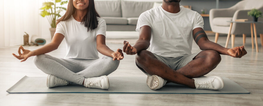 Domestic Yoga. Happy young black couple meditating with closed eyes at home in lotus position, millennial lady and guy sitting on fitness mat on the floor in living room, enjoying healthy lifestyle