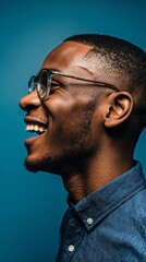 Obraz premium Smiling Man With Glasses Standing Against a Blue Wall in Bright Sunlight