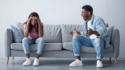 Relationship Problems Concept. Emotional annoyed stressed black couple arguing at home sitting on...