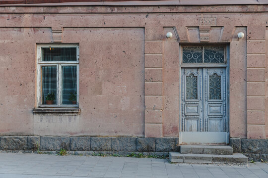 View of a weathered pink building facade with a vintage window and a decorative blue door, evoking a sense of history and quiet charm, Gyumri, Shirak Province, Armenia.