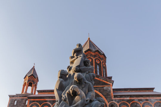View of dark stone monument with figures clustered together against the backdrop of the Church of the Holy Saviour, Gyumri, Shirak Province, Armenia.