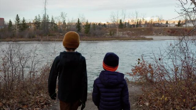 Two young boys walking up to a river shore on a chilly evening