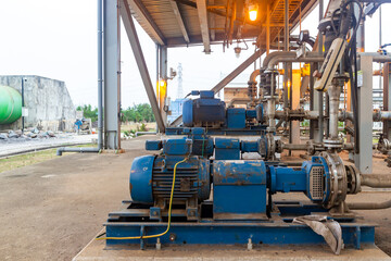 Industrial pumps transferring liquid in factory under roof with pipes. Blue pumps on concrete base. Plant machinery for industrial applications.