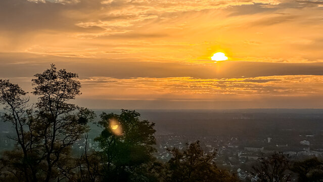 Sunset over a valley with silhouetted trees and vibrant clouds in the evening sky