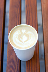 Latte art in a white cup on wooden bench creates a cozy cafe vibe for morning relaxation