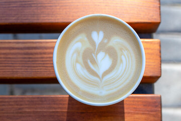 Latte art in a cup featuring heart and rosetta pattern on a warm wooden cafe table