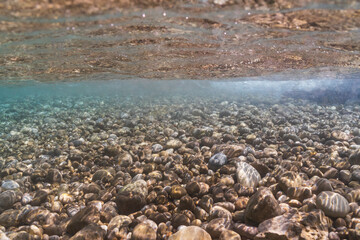 Underwater view of a clear pebble seabed in the shallow turquoise water of Saint-Jean-Cap-Ferrat, French Riviera, France.