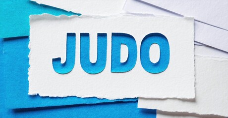 Judo word displayed on torn paper pieces. Blue background creates dynamic visual impact. Simple, direct message.