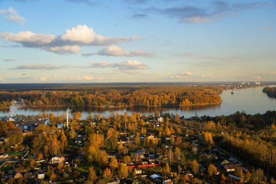 A picturesque scene unfolds with vibrant autumn foliage surrounding a tranquil river. Boats glide across the reflective water as the sun sets, casting warm hues across the sky