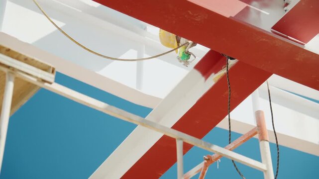 Worker spray-painting a metal structure with white paint using a spray gun on scaffolding