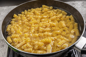 A pan of spiral rotini or fusilli pasta cooking showing bubbling water
