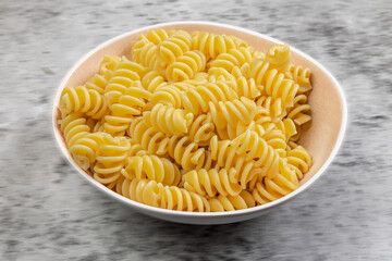 A bowl of cooked spiral rotini or fusilli pasta on a grey tabletop