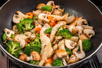 A pan or wok filled with pork stir fry with broccoli and mushrooms