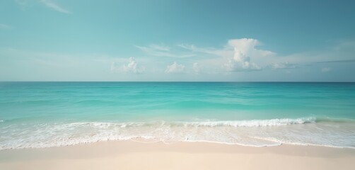 Turquoise ocean meets white sand beach under clear blue sky with scattered clouds. Gentle waves lap shore, creating serene tropical paradise scene. Idyllic coastal landscape invites relaxation,
