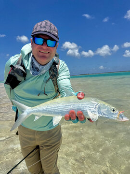 Fly fisherman holding a freshly caught bonefish while standing on the crystal-clear tropical flats of Kiritimati (Christmas Island), Kiribati. This remote Pacific atoll is internationally recognized a