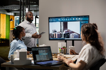 Urban development diverse team discussing property investment new strategy for project approval in a bright office setting, analyzing blueprints and smart city 3D models on architectural software.