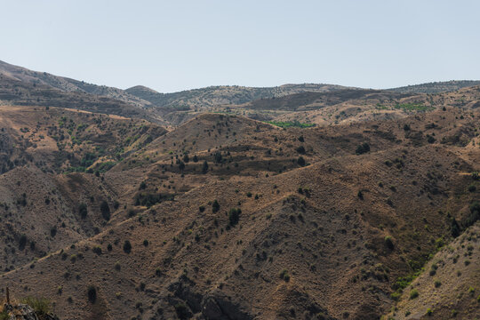 View of sun-baked hills ripple across the landscape under a hazy sky, casting long shadows and revealing textures in Garni, Kotayk Province, Armenia.