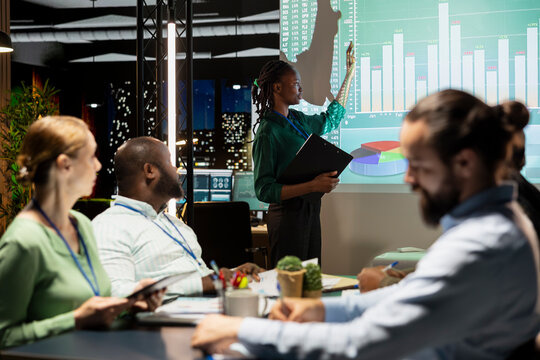 Chief financial officer presenting capital funds and revenue data on annual reports in conference room, reviewing profit increase and budget allocation for new project. After hours late meeting.
