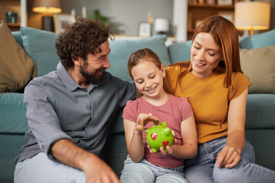 Parents and their daughter sit on a comfortable sofa, engaging joyfully as she plays with a piggy bank, learning the value of saving in a warm and inviting living space.
