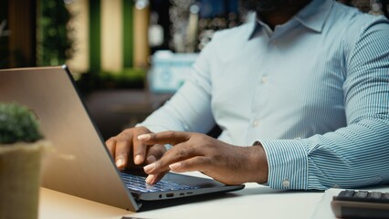 Close up of black worker proofreading and fact checking financial data, reviewing archived files after hours in strategy room. Evaluating reports, researching and organizing agenda.
