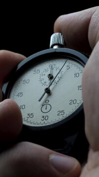 Close-up of male hand activating stopwatch. Idea of performance pressure. Symbol of race against time. Black backdrop emphasizes urgency and concentration in critical moments
