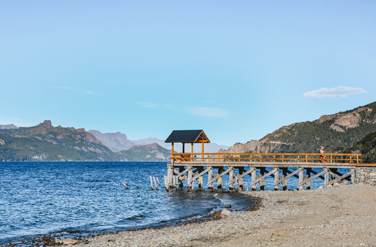 Majestic panoramic view of Lake Traful, surrounded by the dense vegetation of the Patagonian forest. Turquoise blue water framed by imposing mountains and a clear sky. A scene of untouched nature and 