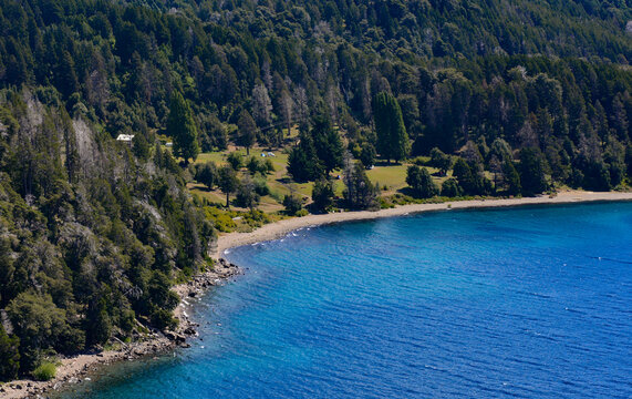 Stunning aerial or viewpoint of a small bay on a Patagonian lake Traful. The intense turquoise water contrasts with the sandy beach and the lush forest covering the mountain slopes under a clear sky.